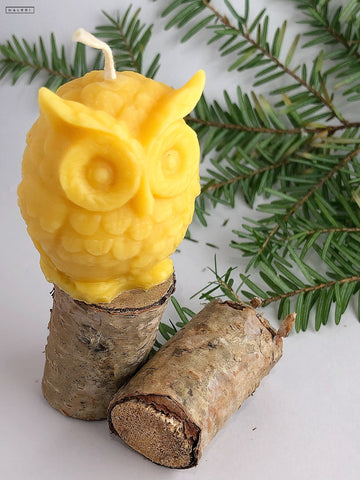 a small pure beeswax candle in the shape of an owl rests upon a tiny wooden log