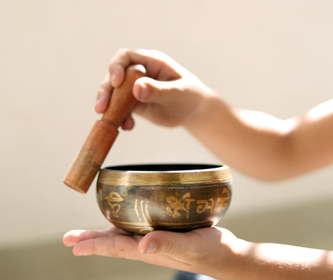 a plays a tibetan singing/sound bowl while holding it in their hand