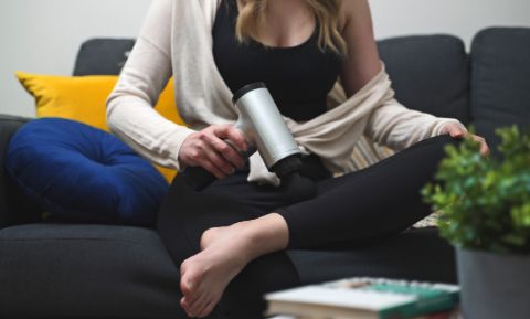 Woman sitting on a couch massaging her calf muscle with a percussion massage gun