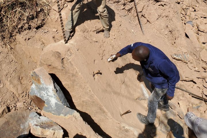 Zimbabwean miners hammering pins into a large rock to break it into smaller pieces
