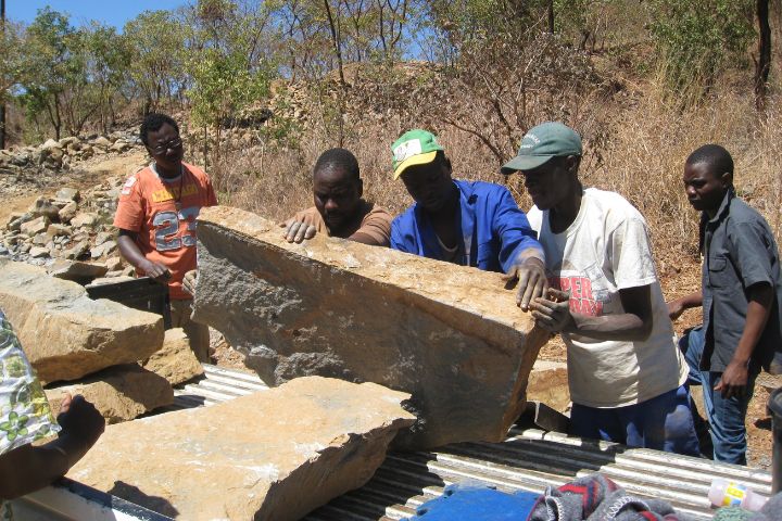 Zimbabwean miners holding up a large springstone boulder