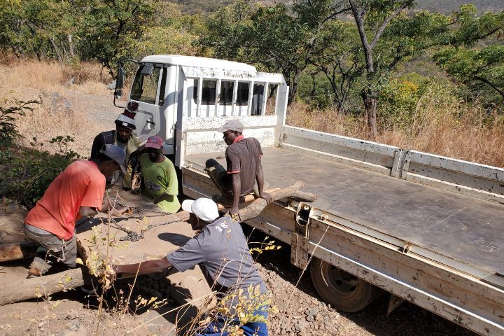 Zimbabwean miners using logs to move large stones into a truck