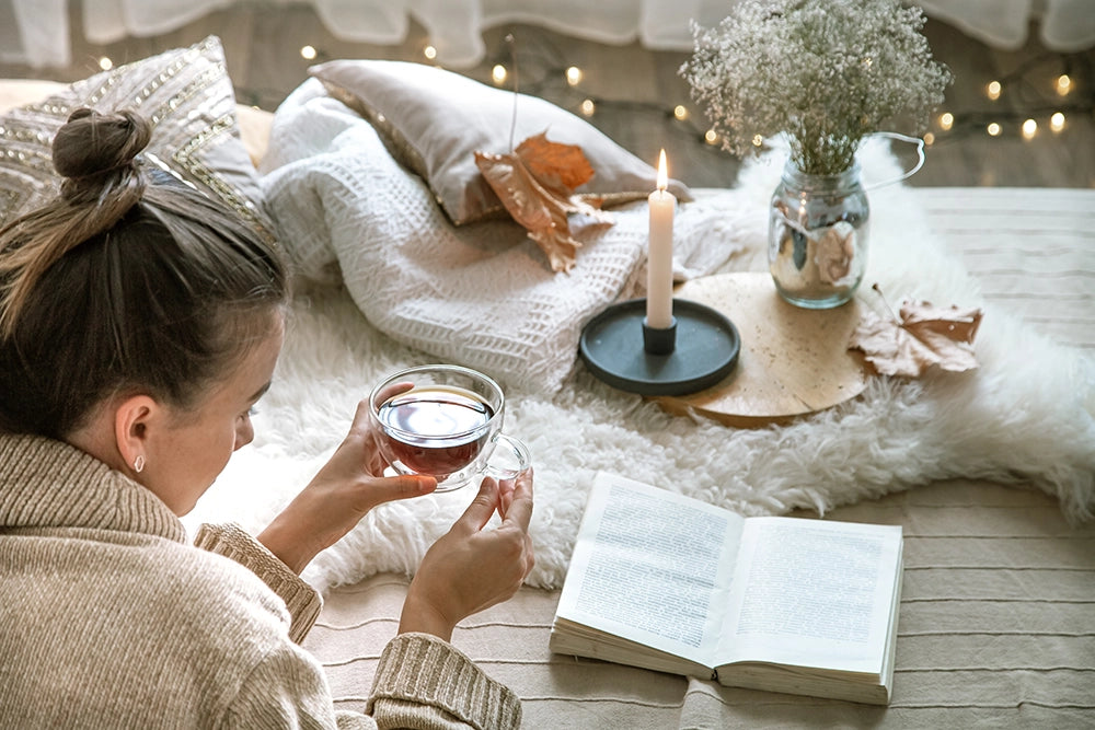 Femme lisant un livre dans un décor cocooning d’hiver avec une tisane à la main