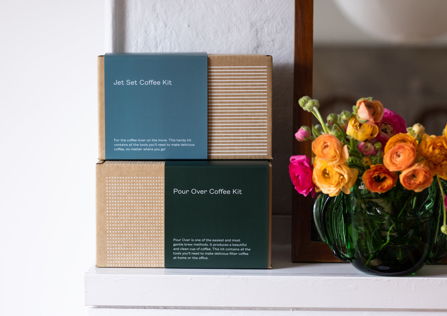 Two coffee kit boxes stacked on top of each other sitting next to a vase full of flowers. The bottom box is a Pour Over Coffee Kit and the top is a Jet Set Coffee Kit.