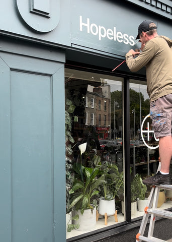 Andrew from Wonder and signs - a man in shorts painting signage on Hopeless Botanics new shop