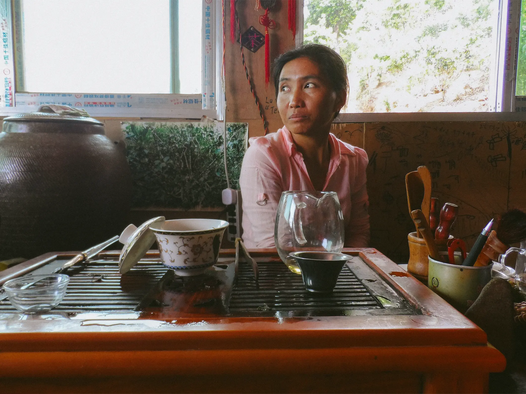 Woman Sat Looking Contemplative by a Window with a Tea Set in-front of Her