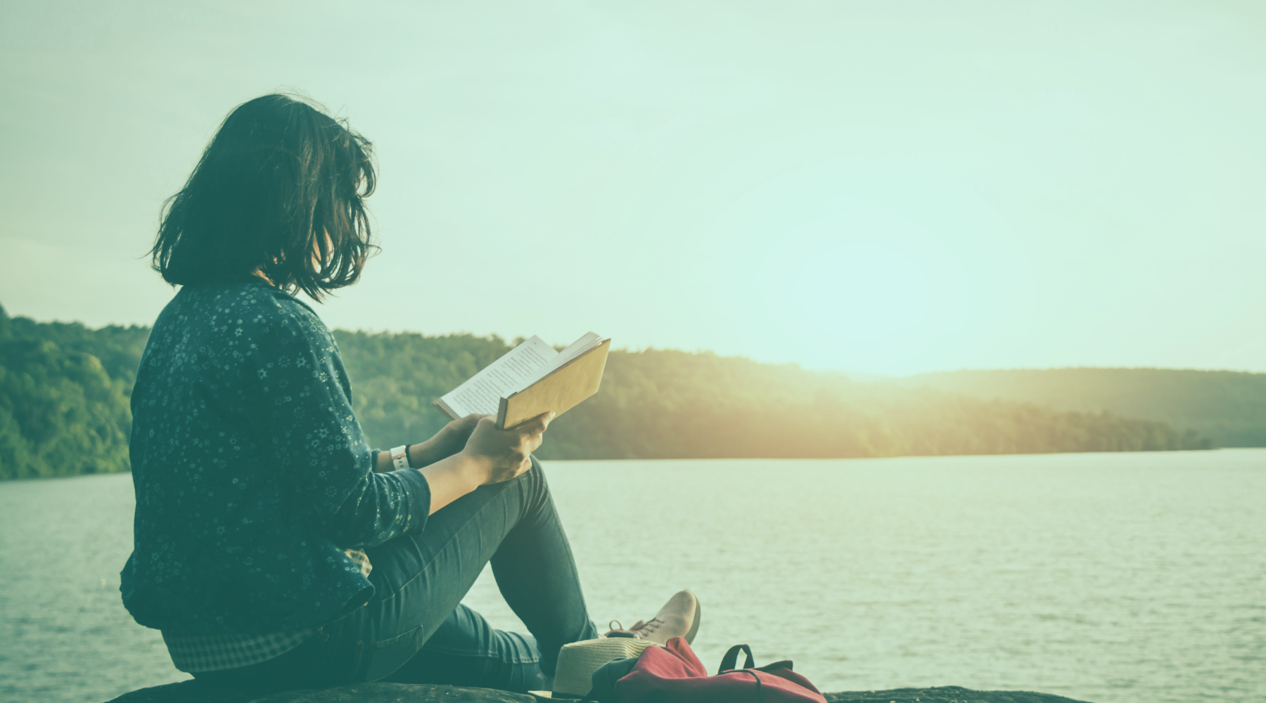 Frau liest aus Journal am See mit Bergen im Hintergrund