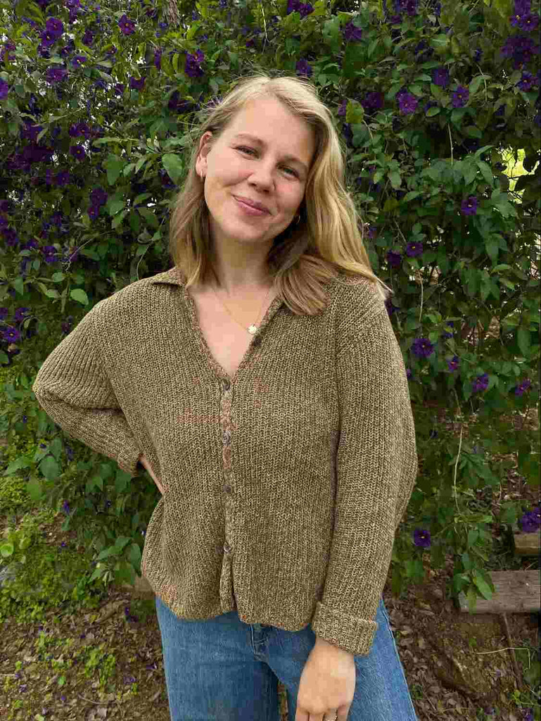 Woman with medium blonde hair in a garden wearing a green long sleeved shirt and denim jeans