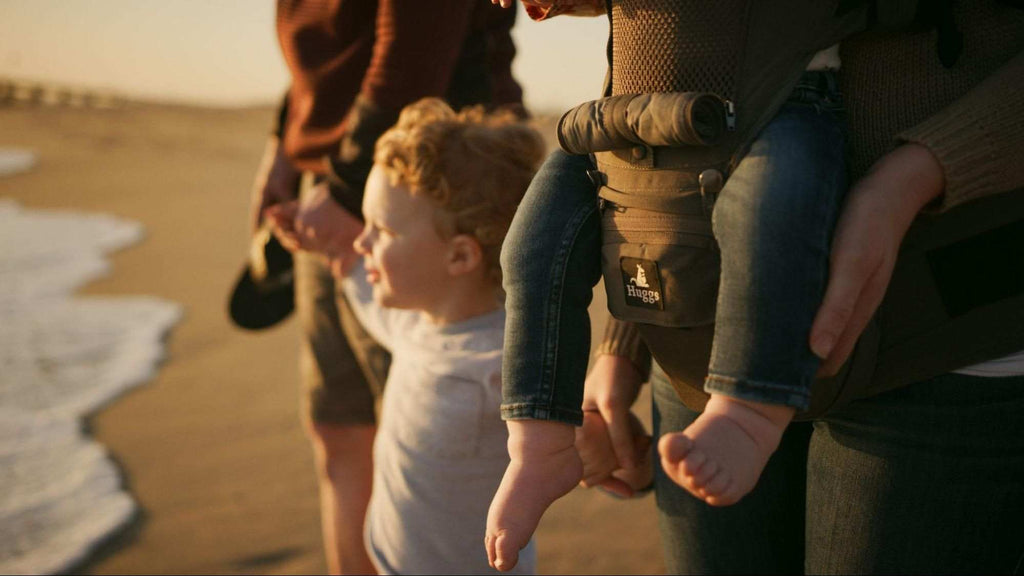 family using a huggs front carrying baby carrier at the beach