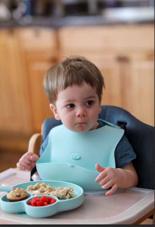 Baby in Abiie high chair and bibb eating out of Abiie plate