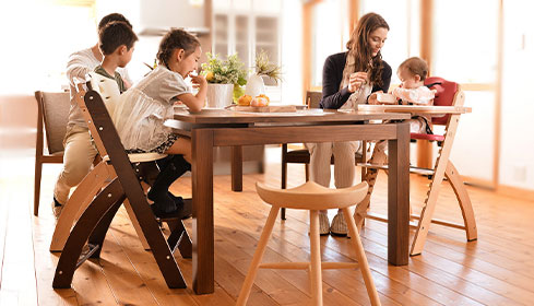 family around table while mom feeds baby in modern wooden high chair