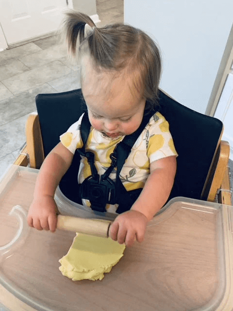 girl rolling dough in high chair