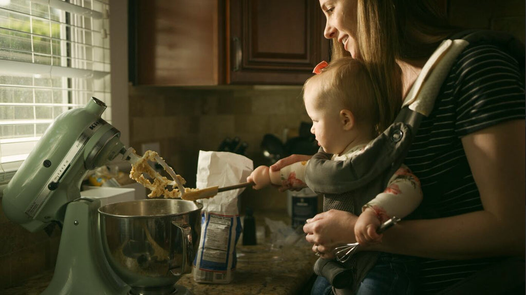 Mom holding her baby in the Huggs Baby Carrier while cooking