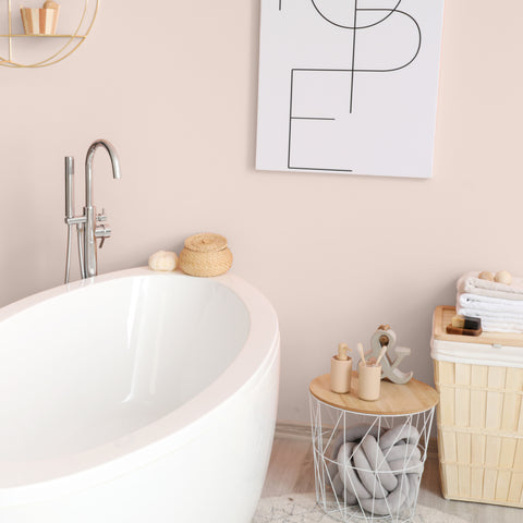 light pink bathroom painted in Colourtrend Paints shade Iced Float. White bath, white graphic print on the wall, light rattan laundry basket in the corner.