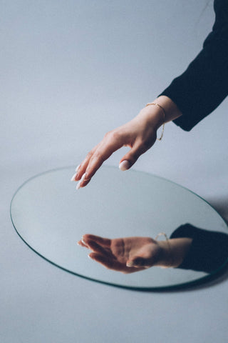 Person in black long sleeves trying to touch a circular mirror