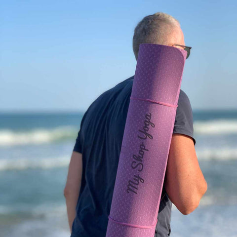 homme yogi marche sur la plage avec son tapis de yoga sur l'épaule