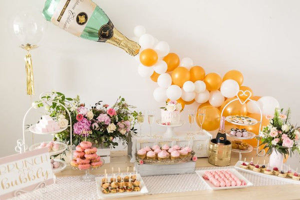 Bridal Shower Theme Idea: Brunch and Bubbly. Balloons of champagne popping along the wall. Table with: Pink 'Brunch and Bubbly' sign on the table, blush toned floral arrangement, chilled champagne bottle,  desserts and finger food.