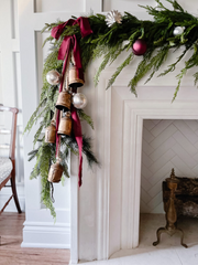 A white mantel  decorated with christmas garland, bells, and red ribbon. 