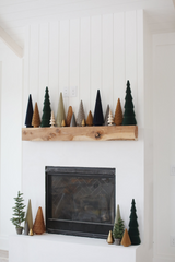 Woodland Christmas Mantel Decorations: clay christmas trees in earth tones sitting on a white mantel.  There are clay Christmas trees placed near the fireplace. 