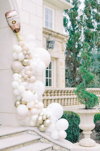 White, cream, and light pink balloon bouquet. Champagne balloon on top. Leaning up the steps of a building (outside). 