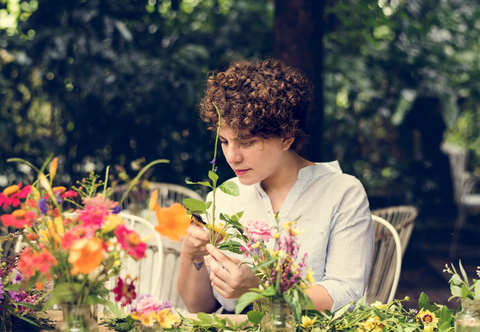 A woman sitting outside at a table, creating flower arrangements. 