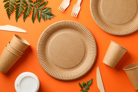 From a top down view, bamboo plates, cups, and utensils are set against an orange background.