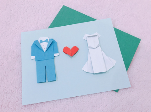 A dropdown shot of invitations. The invitations are blue with a paper groom's suit, heart, and white bridal dress.