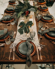 Woodland Christmas Table Setting: dark brown wooden table, gold metallic cutlery, mix and match glasses, copper plates with forest green linen napkins, greenery and candle decor, and a white knitted table runner. 