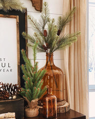 Boho Christmas Decoration. A copper transparent jar shaped vase with branches of pine and pine cones. Sitting on a dresser in a bohemian styled room.