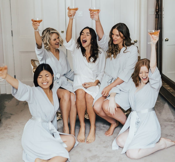 Bridal Shower Theme Ideas: Slumber Party. Five women in bathrobes cheersing. Four women are wearing blue bathrobes and one is wearing a white one.