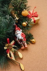 Festive Christmas ornaments hanging off a tree thats laying on a cork floor. There is a golden music note with a red bow, a Santa figure, gold bulbs, a bell, and a small gift near the tree.