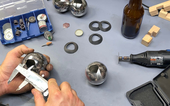 Two hands measure a prototype of the Convex bottle opener on a blue counter top surrounded by tools and parts. 