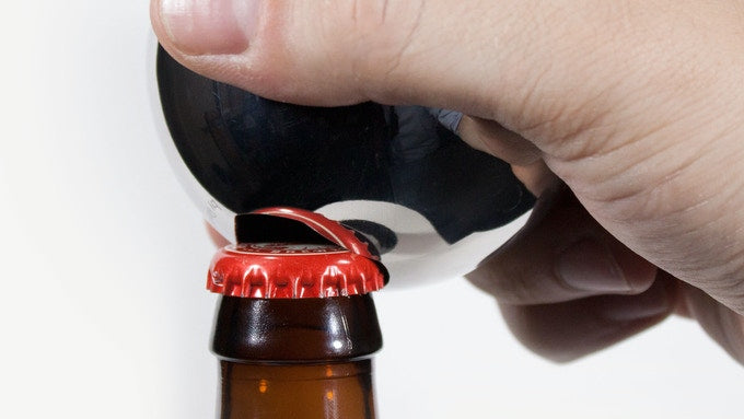 A hand prys a red bottle top off of a brown bottle. 