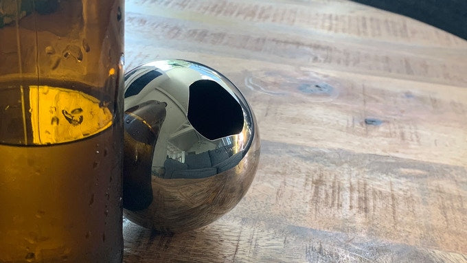 A stainless steel bottle opener hides behind a brown bottle on a wooden coffee table.