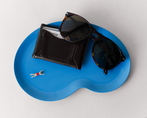 Marco Tray in swimming pool blue desinged by Revision holding a black wallet and sunglesses on a grey background. 