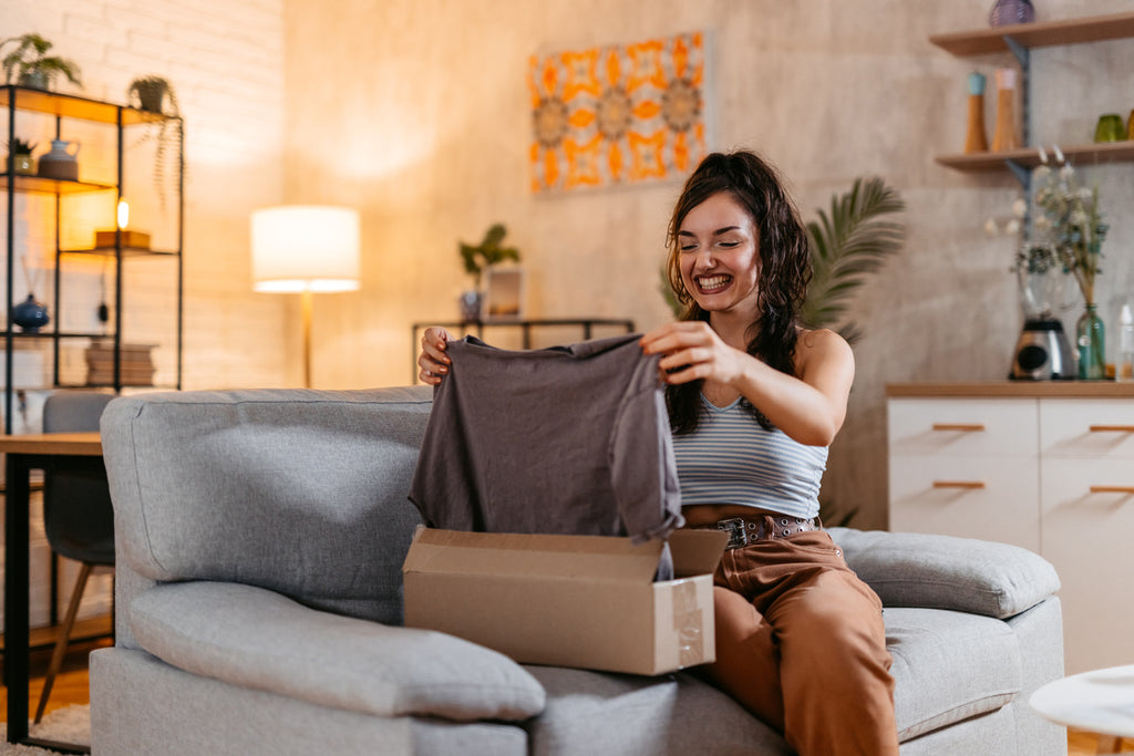 young cheerful woman unboxing a package in the living room of a new t-shirt.