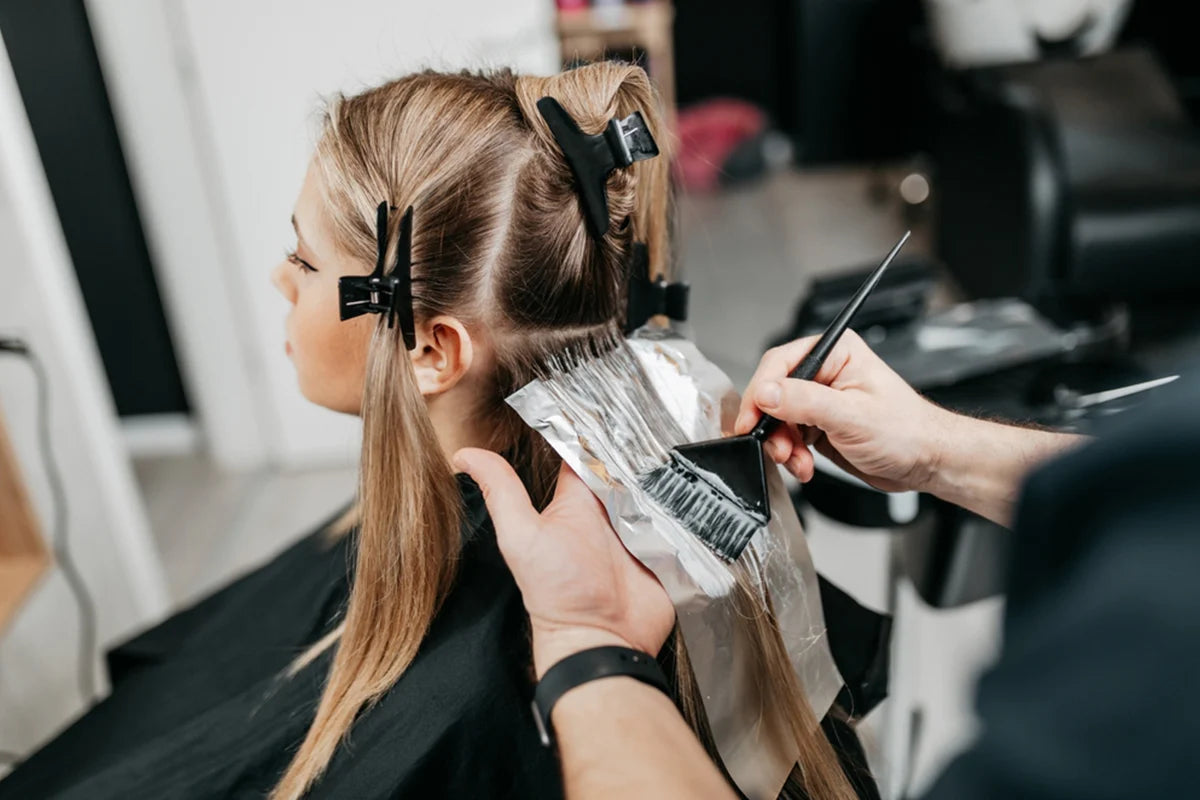 Hair stylist applying GK Hair Treatment to a girl's hair in a salon setting.