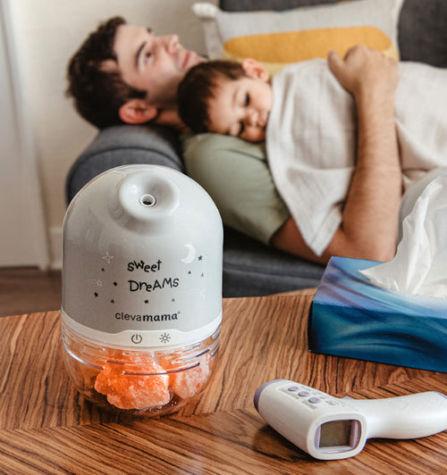 an humidifier and thermometer over a table with a person with a baby lying on a couch in the background
