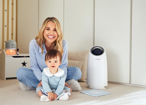 Vogue williams sitting on the floor with a baby next to an air purifier