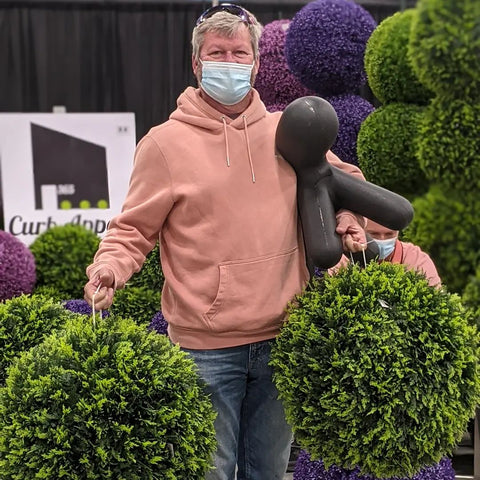 Customer carrying large boxwood style artificial topiaries