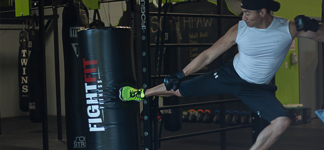 Man kicking a freestanding bag that has the FightFit logo on it