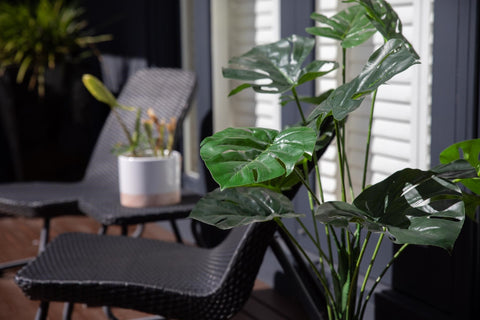 Green artificial tropical plant on sunny patio in pot
