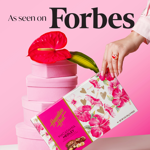 Hawaiian Host Valentine's Picture As Seen on Forbes on Pink background with heart shaped boxes red anthurium and Hawaiian Host Macadamia Medley Box with pink hibiscus and gold hearts on the box cover