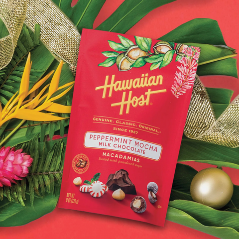 Hawaiian Host Peppermint Mocha Milk Chocolate on red background topped on monstera leaf, birds of paradise, pink ginger, and gold ribbon and ornament