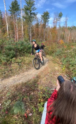 Photographer photographing women mountain biking in colorful fanny packs