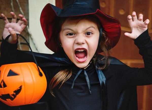 Girl in witch costume holding a Halloween pumpkin basket