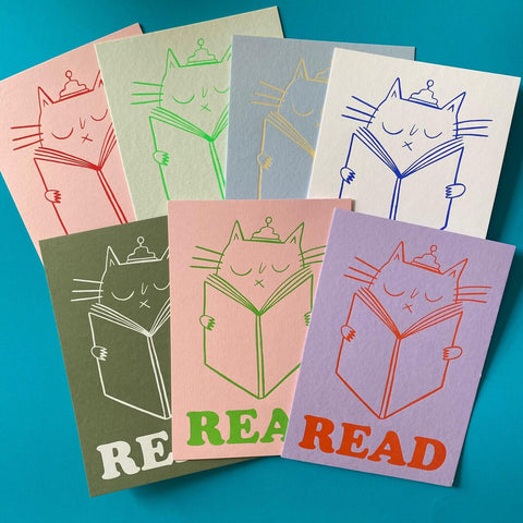 5 differently coloured prints showing a cat reading and the word READ