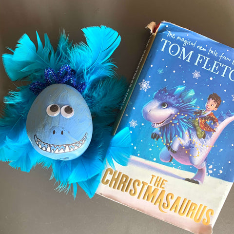 A potato decorated as The Christmasaurus next to the book The Christmasaurus by Tom Fletcher