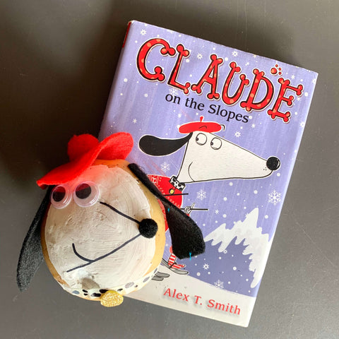 A potato decorated to resemble Claude the dog, next to the book Claude on the Slopes