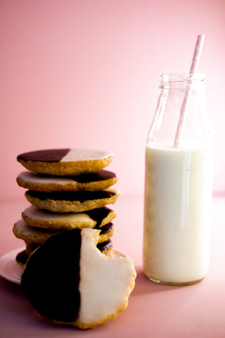 Vertical photo of a stack of Black-and-white cookies next to a glass bottle of milk